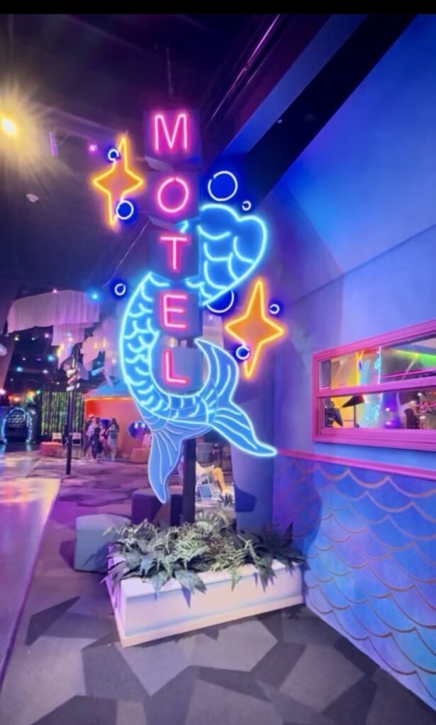 Neon motel sign with a glowing mermaid tail inside an indoor immersive art attraction
